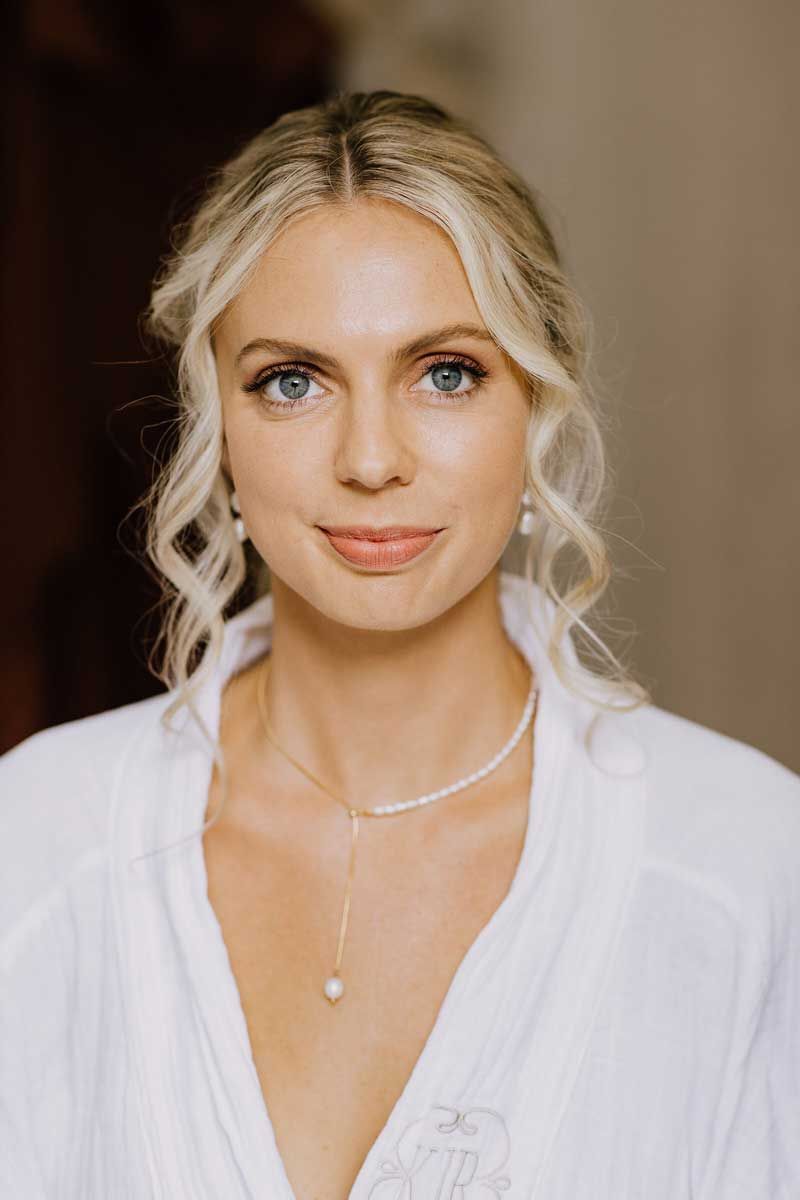 A woman is wearing a white robe and a pearl necklace.