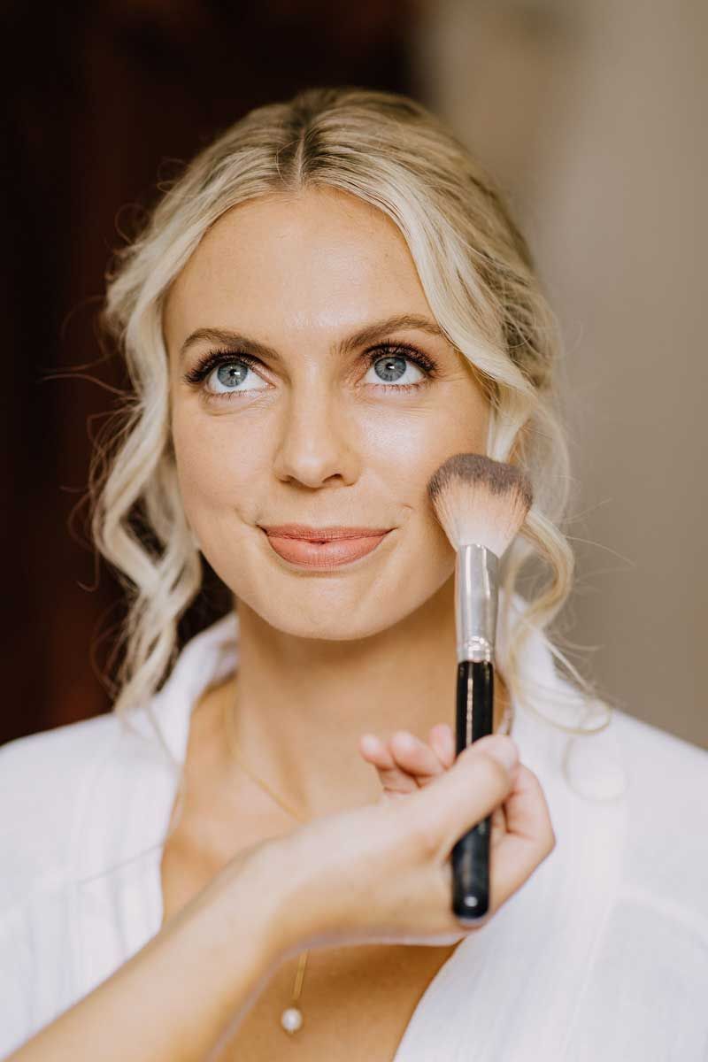 A woman is applying makeup to her face with a brush.