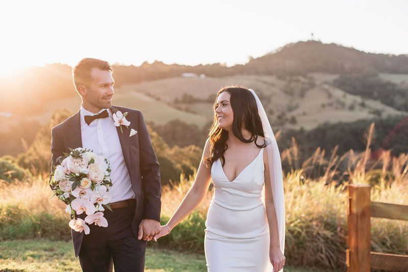 A bride and groom are holding hands while walking in a field.