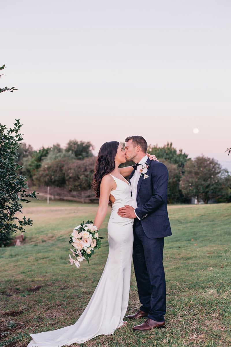 A bride and groom are kissing in a field.