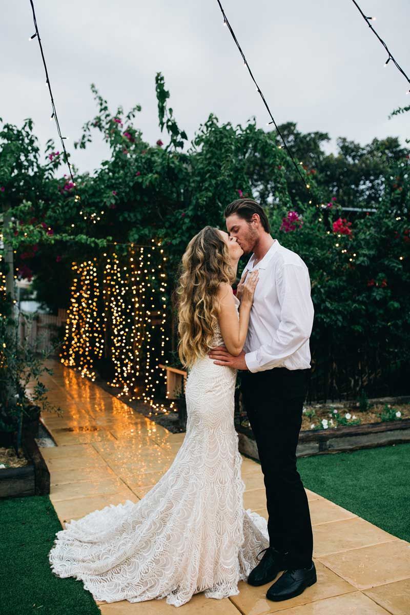 A bride and groom are kissing in front of a wall of lights.