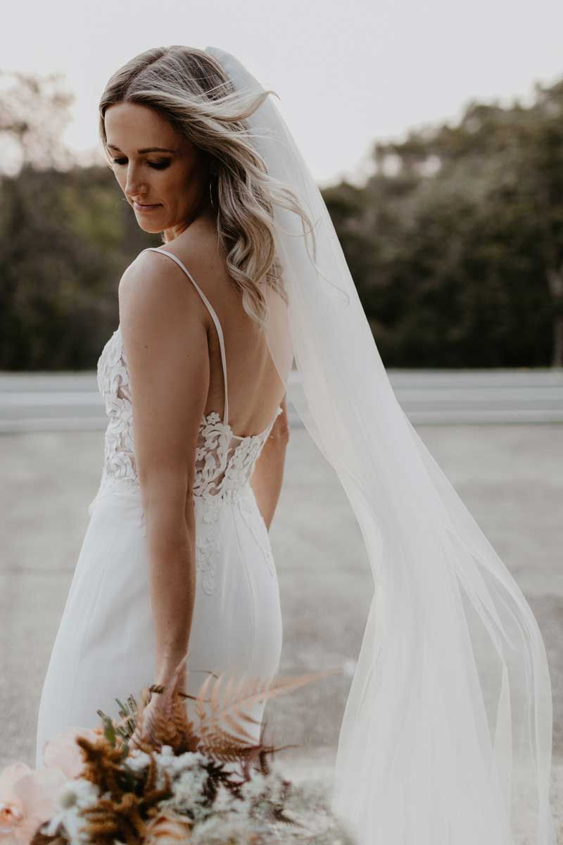 The bride is wearing a long veil and holding a bouquet of flowers.