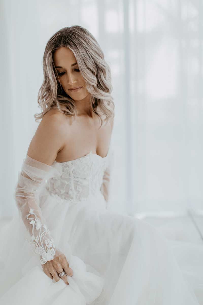 A woman in a white dress and gloves is standing in front of a window.
