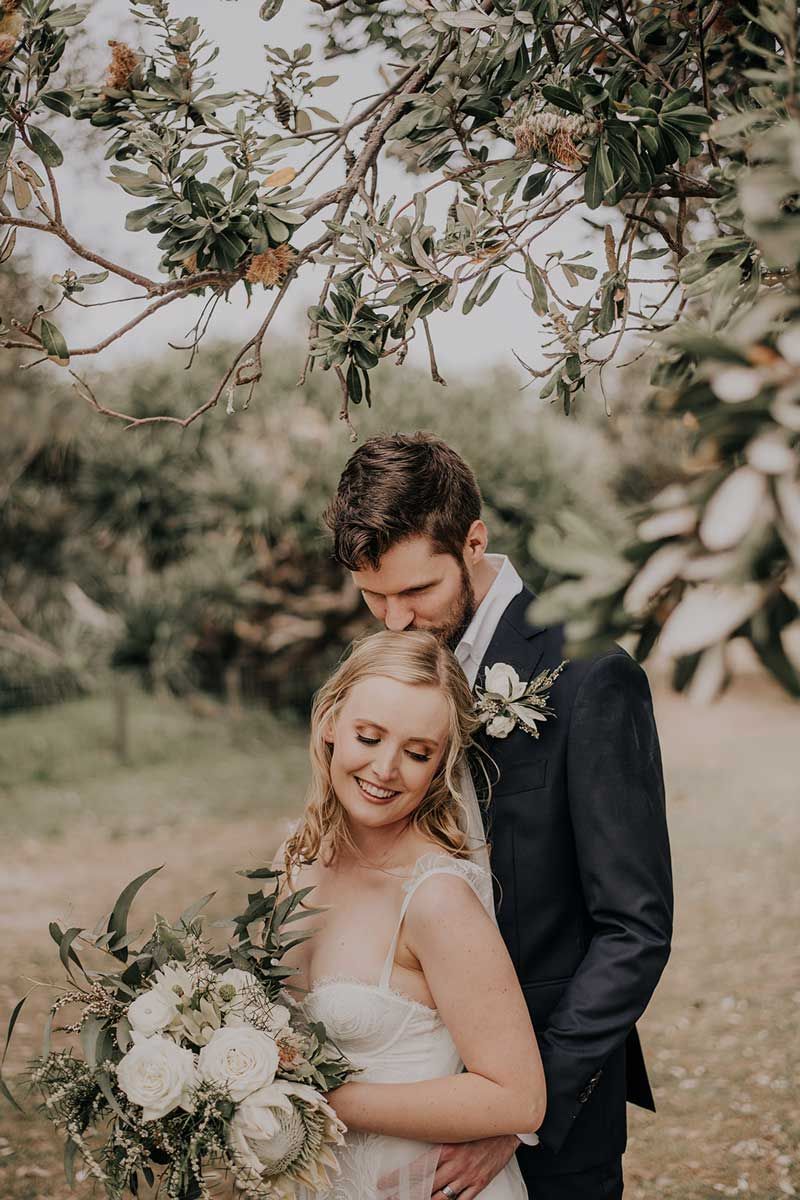 A bride and groom are posing for a picture under a tree.