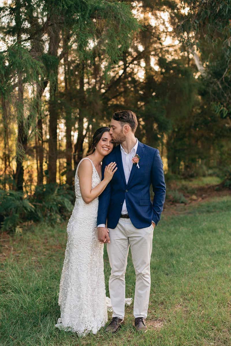 A bride and groom are standing next to each other in a field holding hands.