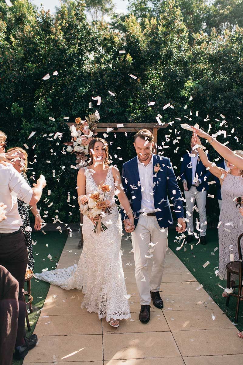 A bride and groom are walking down the aisle while confetti is being thrown at them.