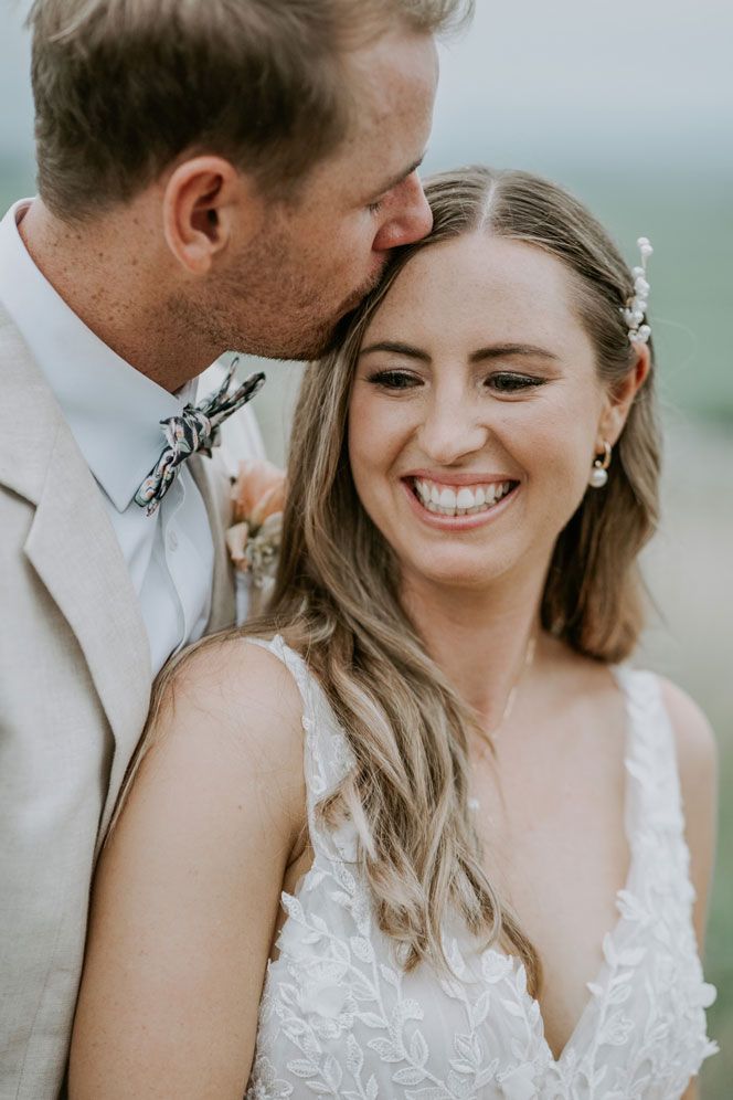 A man is kissing the forehead of a smiling bride.