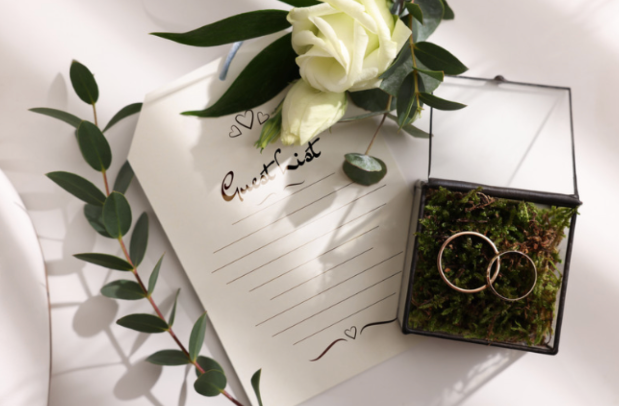 A couple of wedding rings in a box next to a wedding invitation