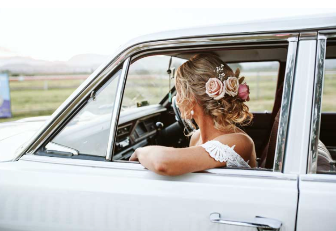 A bride is sitting in a white car with flowers in her hair.