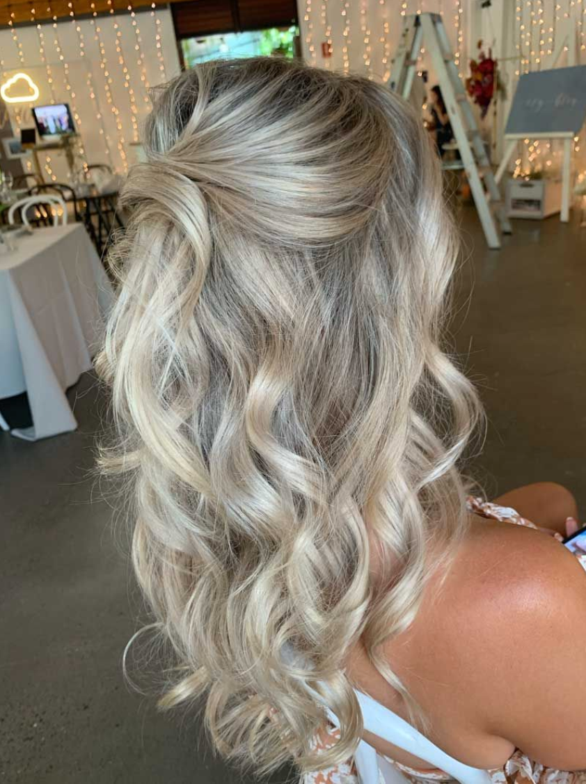 A woman with blonde hair is sitting in a chair with her hair in a half up half down hairstyle.