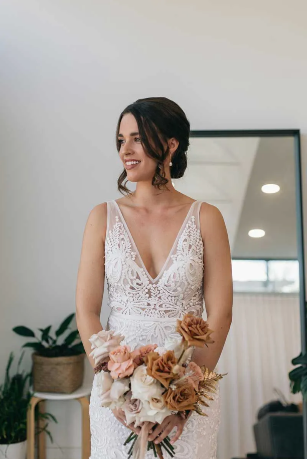 A woman in a wedding dress is holding a bouquet of flowers in front of a mirror.