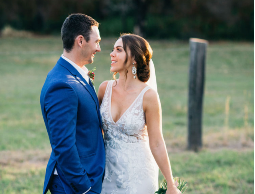 A bride and groom are standing in a field looking at each other.