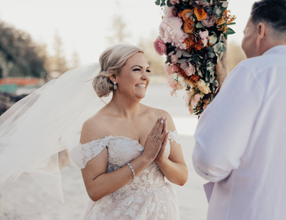 A bride and groom are smiling during their wedding ceremony on the beach.