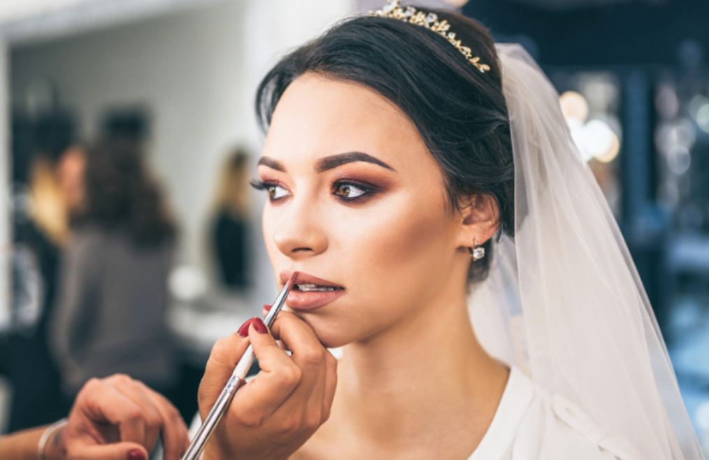 A bride is getting her makeup done by a makeup artist in a salon.