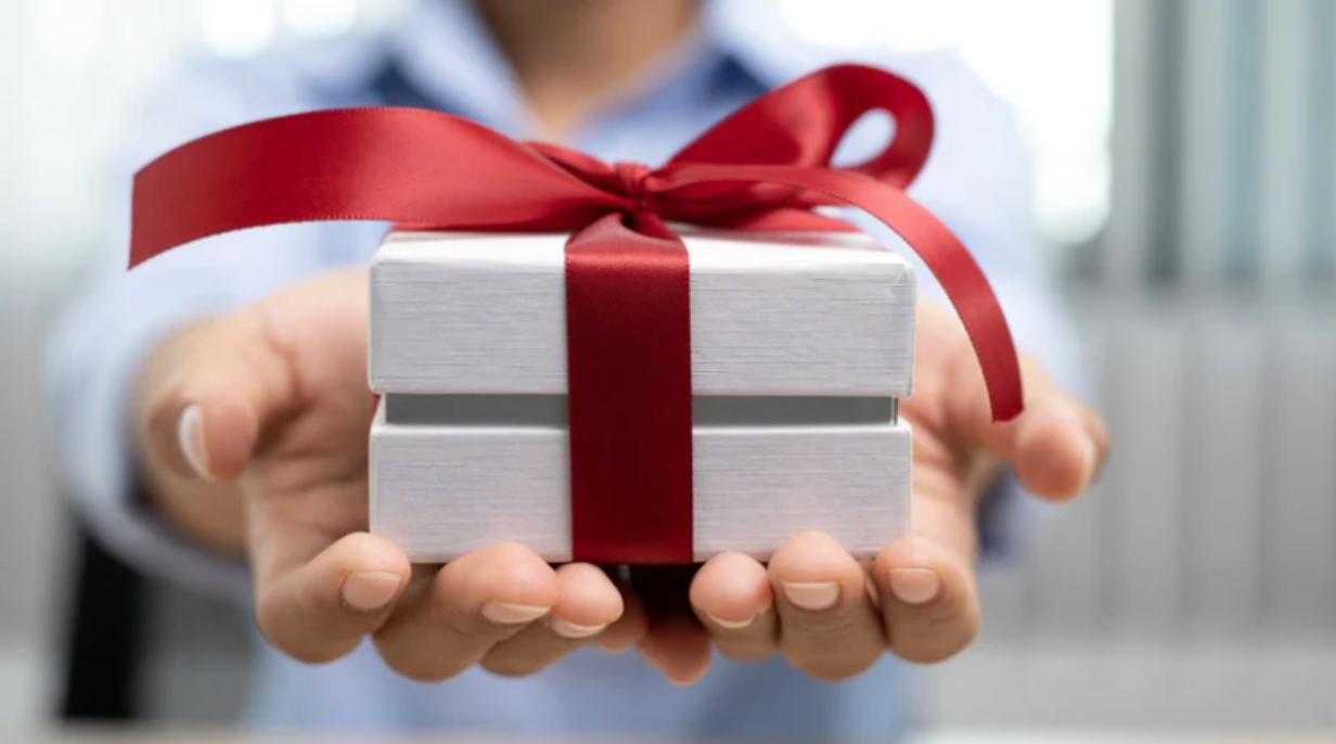 A person is holding a white gift box with a red ribbon.