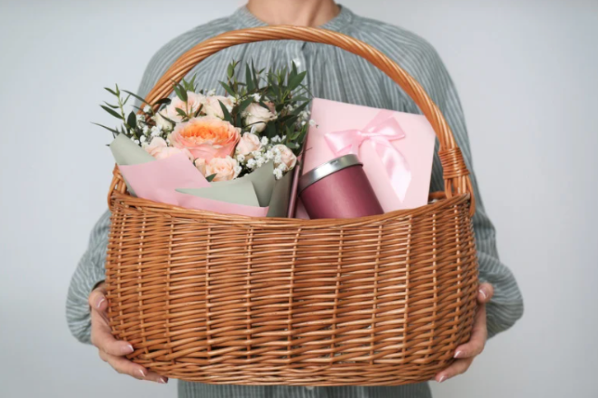 A woman is holding a wicker basket filled with flowers and a cup.