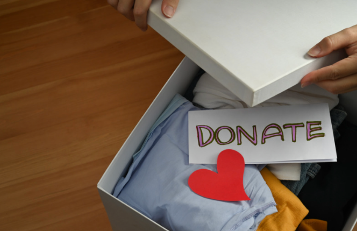 A person is holding a box of clothes with a card that says donate on it.