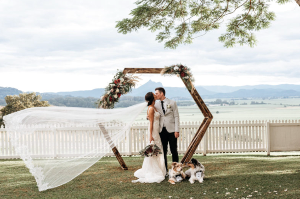 A bride and groom are kissing under a wooden arch at their wedding.