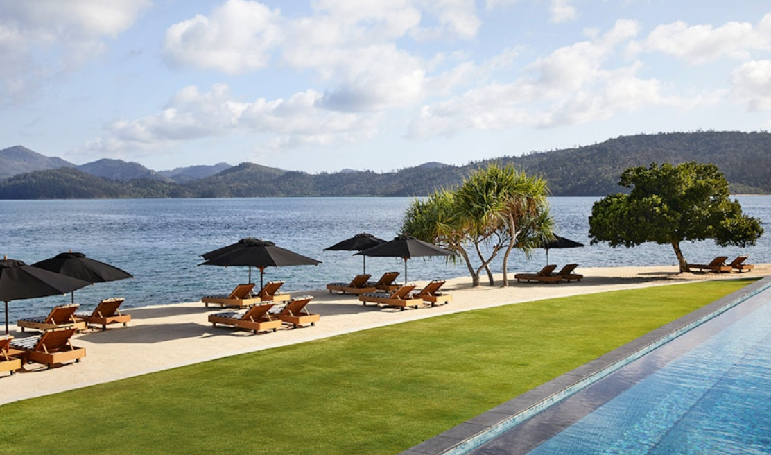 A swimming pool surrounded by chairs and umbrellas next to a body of water.