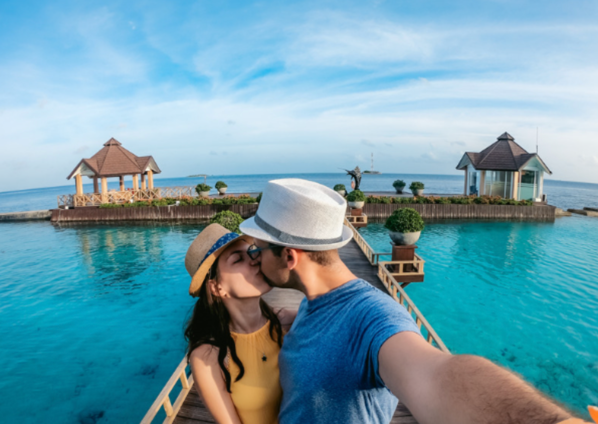 A man and a woman are kissing on a dock overlooking the ocean.