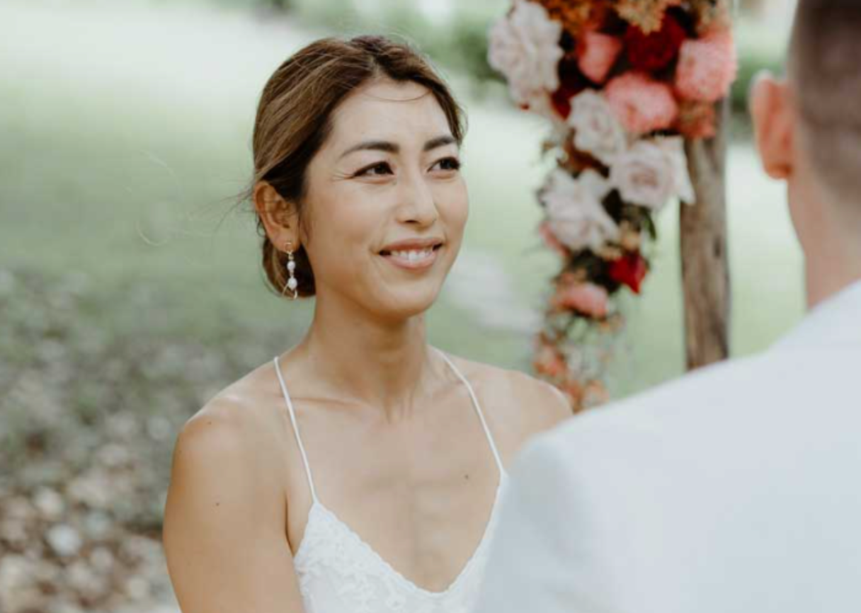 A woman in a white dress is smiling at a man during a wedding ceremony.