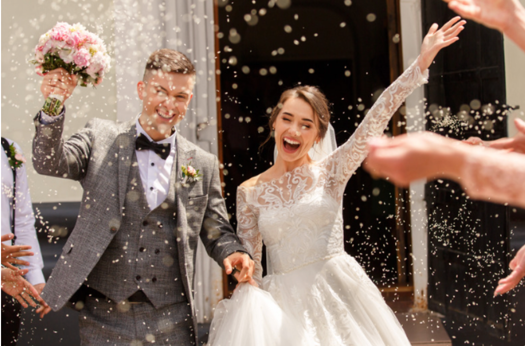 A bride and groom are walking out of a church surrounded by confetti.