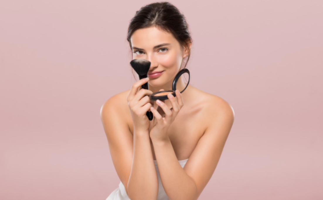 A woman is applying makeup with a brush and a mirror.