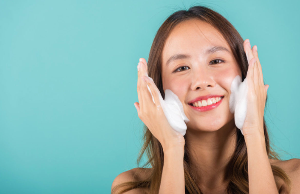 A woman is washing her face with soap and smiling.