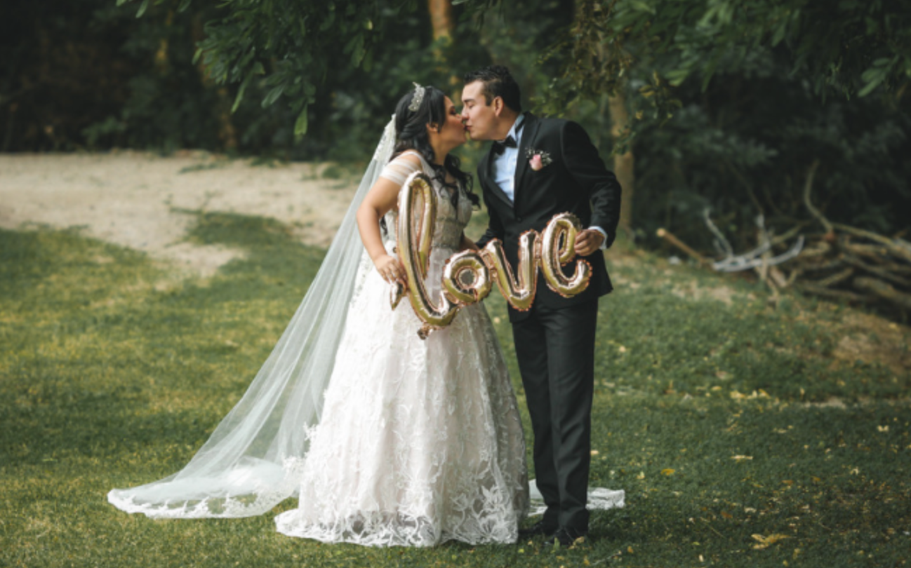 A bride and groom kissing while holding balloons that say `` love ''.