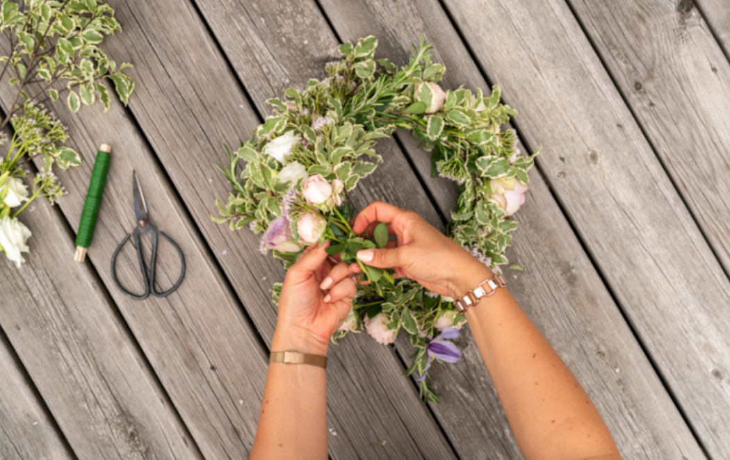 A woman is making a flower wreath on a wooden deck.