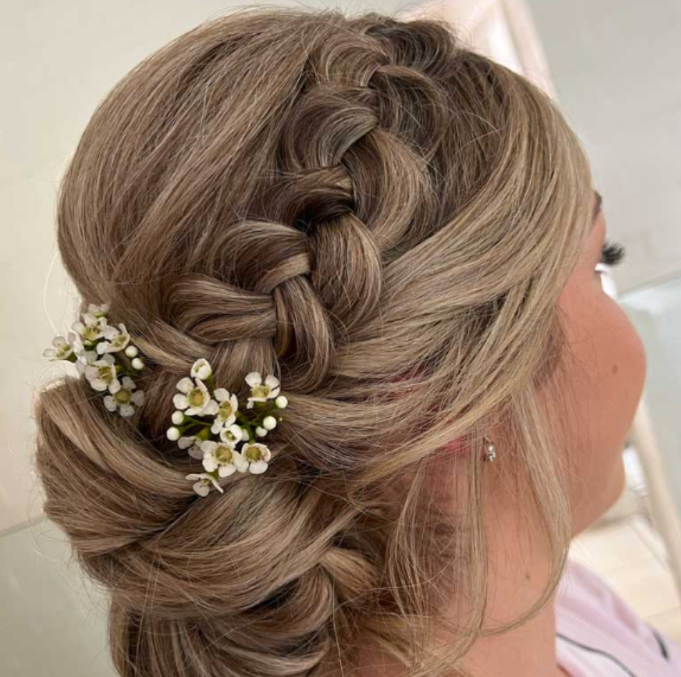 A woman is wearing a braided bun with flowers in her hair.