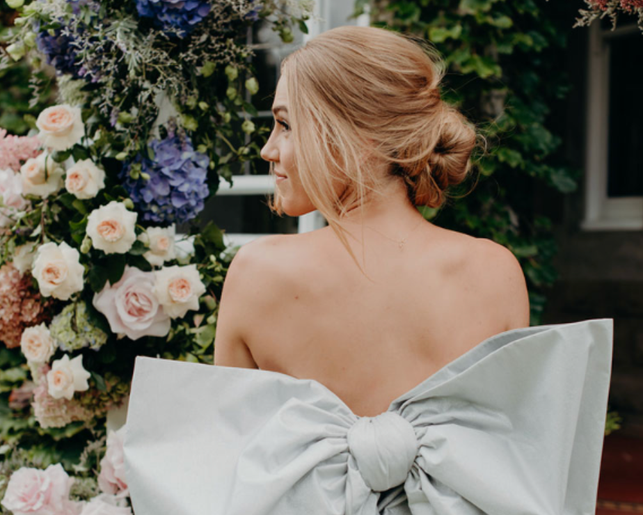 A woman is wearing a white dress with a large bow on the back.