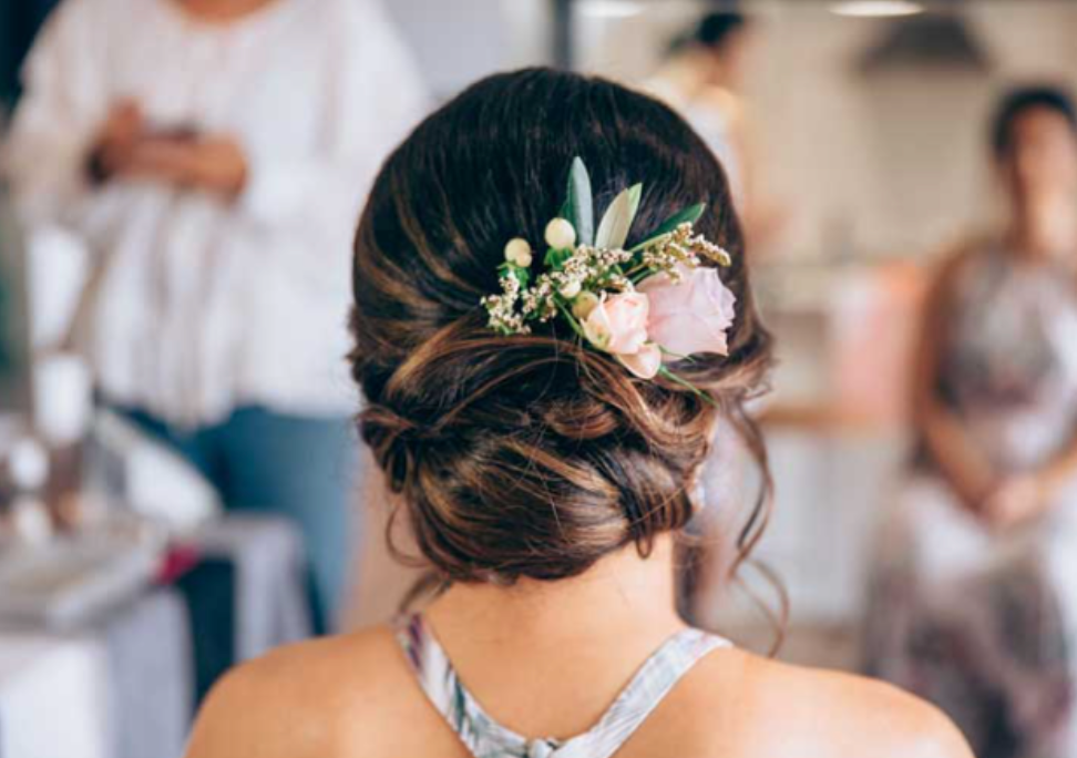 The back of a woman 's head with a bun and flowers in her hair.