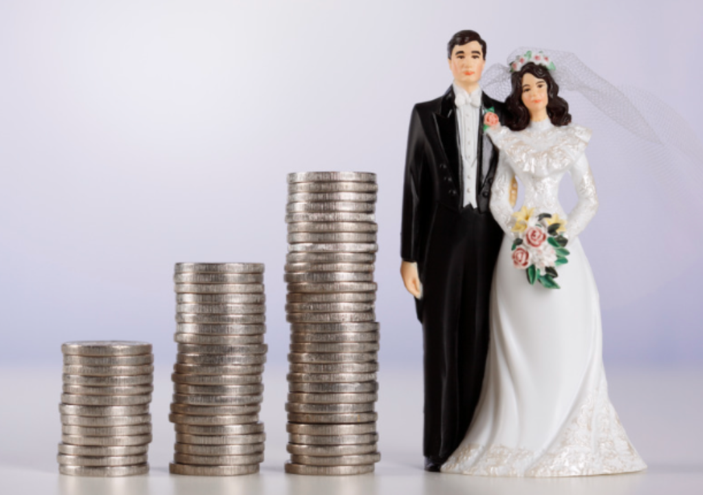 A bride and groom figurine standing next to stacks of coins.