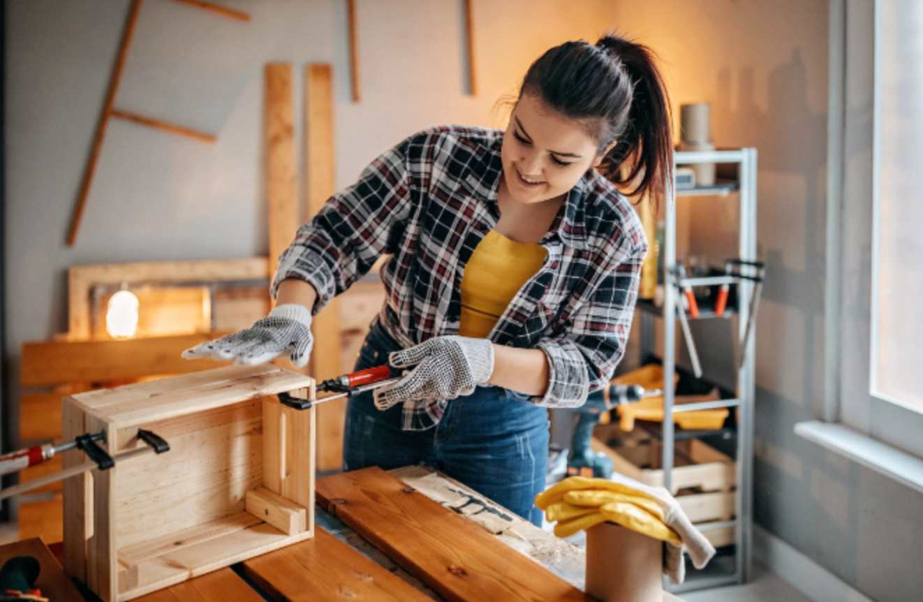 A woman is working on a wooden box in a room.