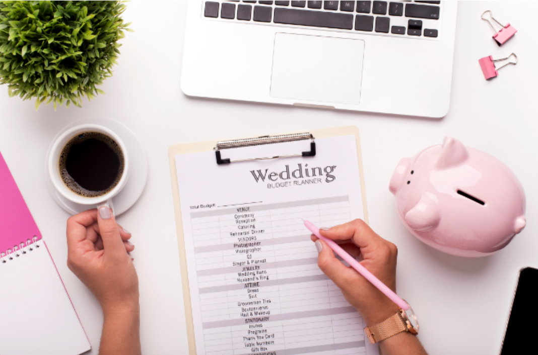 A woman is writing on a clipboard next to a piggy bank and a laptop.