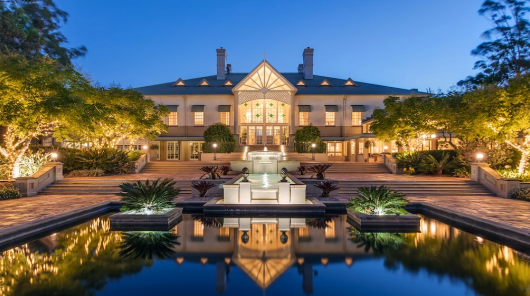 A large house with a fountain in front of it is lit up at night.