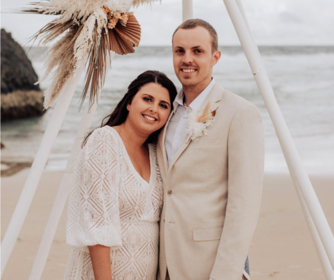 A bride and groom are posing for a picture on the beach.