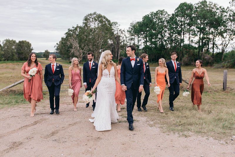 A bride and groom are walking down a dirt road with their wedding party.