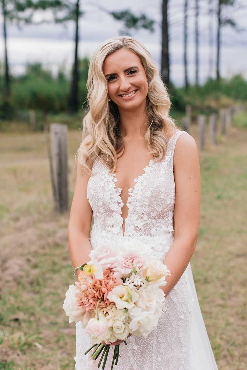A woman in a wedding dress is holding a bouquet of flowers in a field.