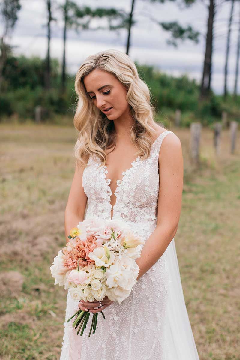 A woman in a wedding dress is holding a bouquet of flowers in a field.