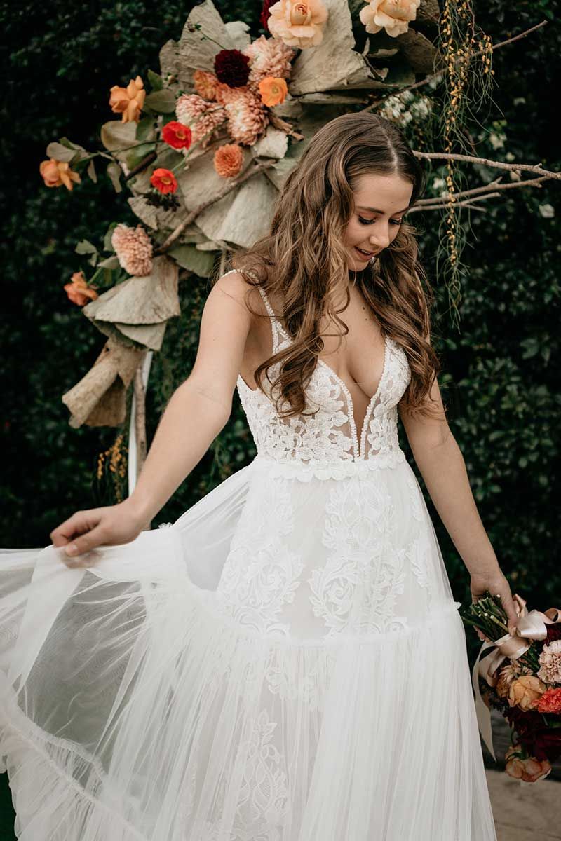 A woman in a white wedding dress is standing in front of a floral arch.