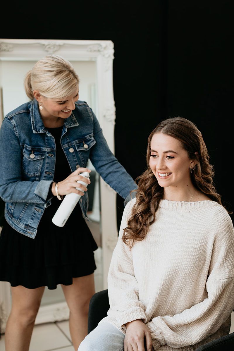 A woman is spraying a woman 's hair in a salon.