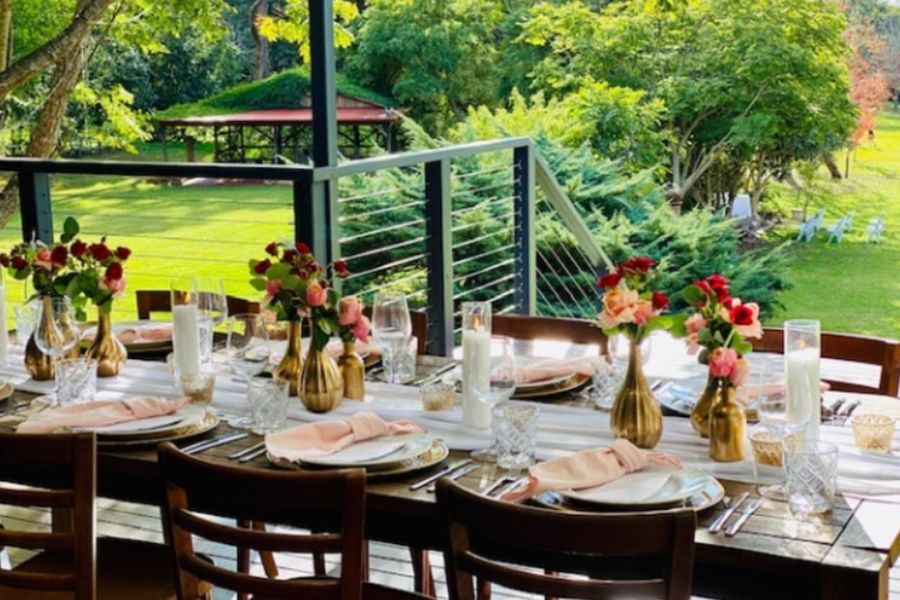 A long table with plates , glasses , and vases of flowers on it.