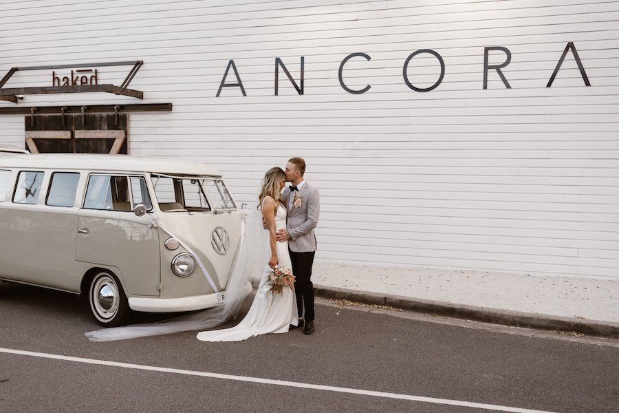 A bride and groom are kissing in front of a white van.