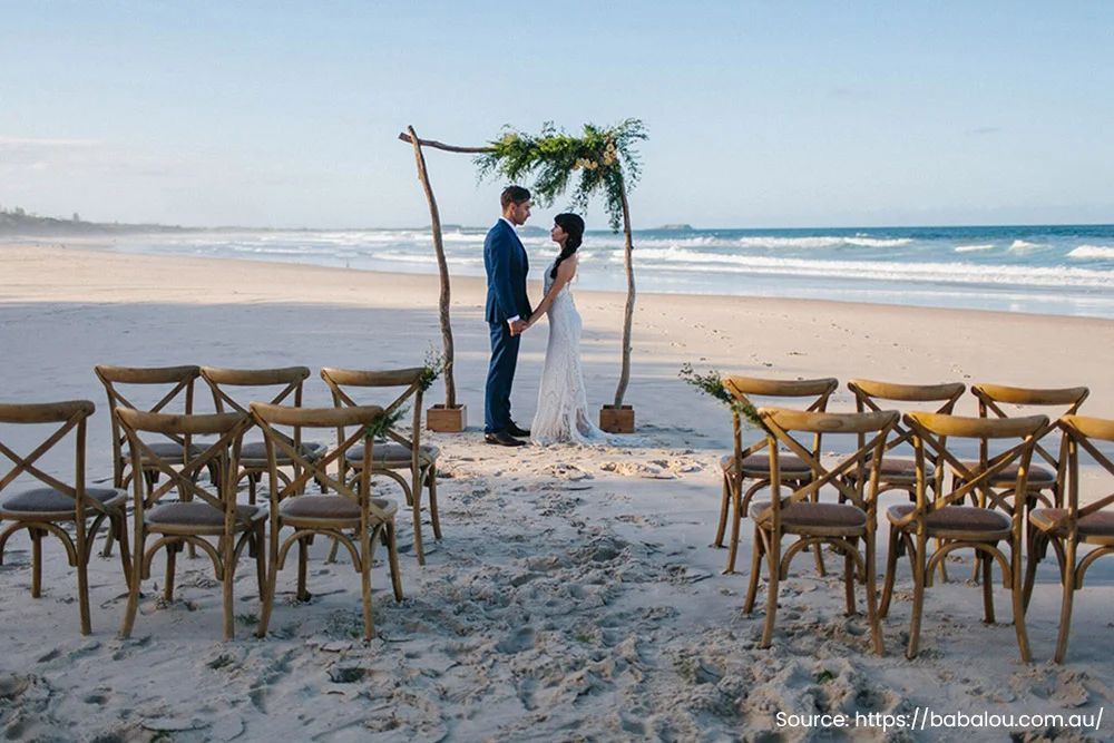 A bride and groom are kissing on a wooden dance floor in a large room.