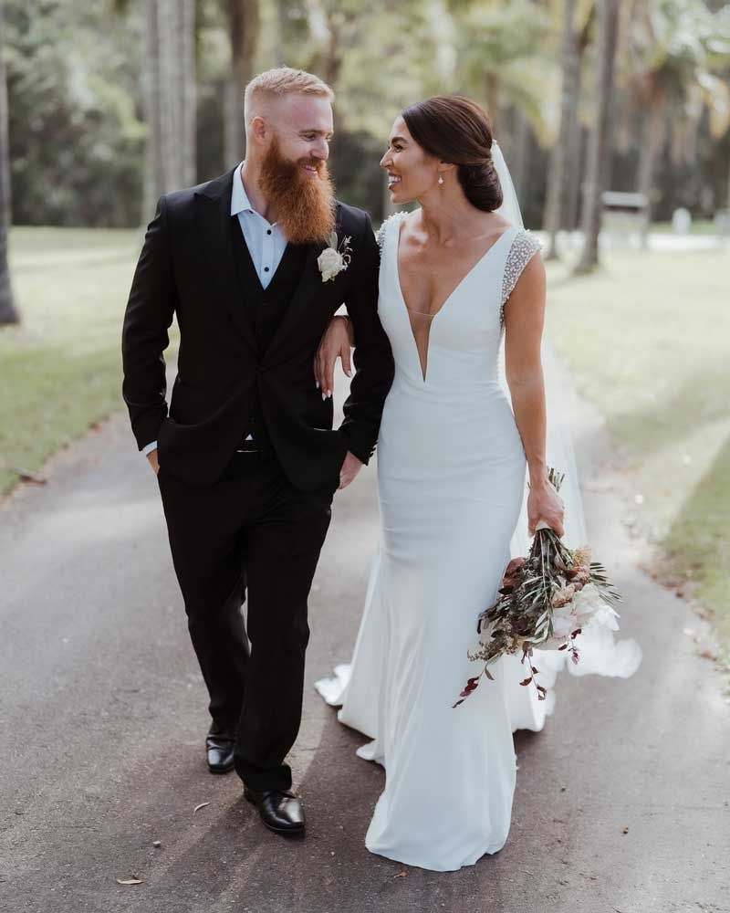 A bride and groom are walking down a path holding hands.