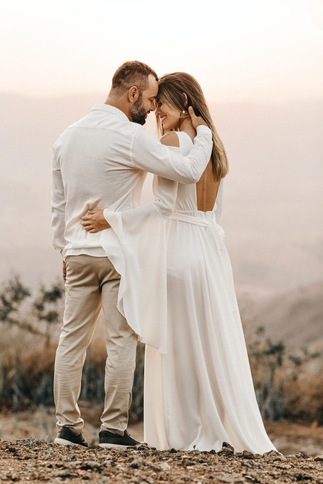A bride and groom are hugging each other on top of a rocky hill.