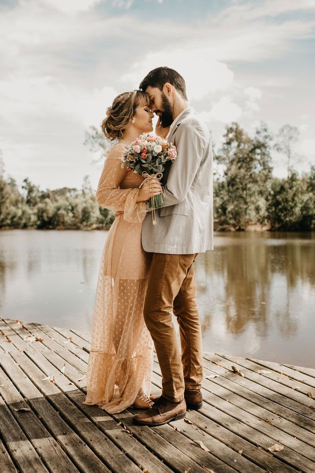A bride and groom are kissing on a dock near a lake.