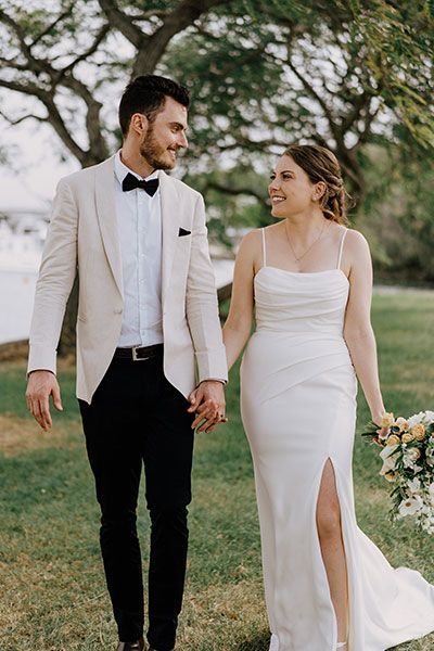 A bride and groom are holding hands while walking in a field.